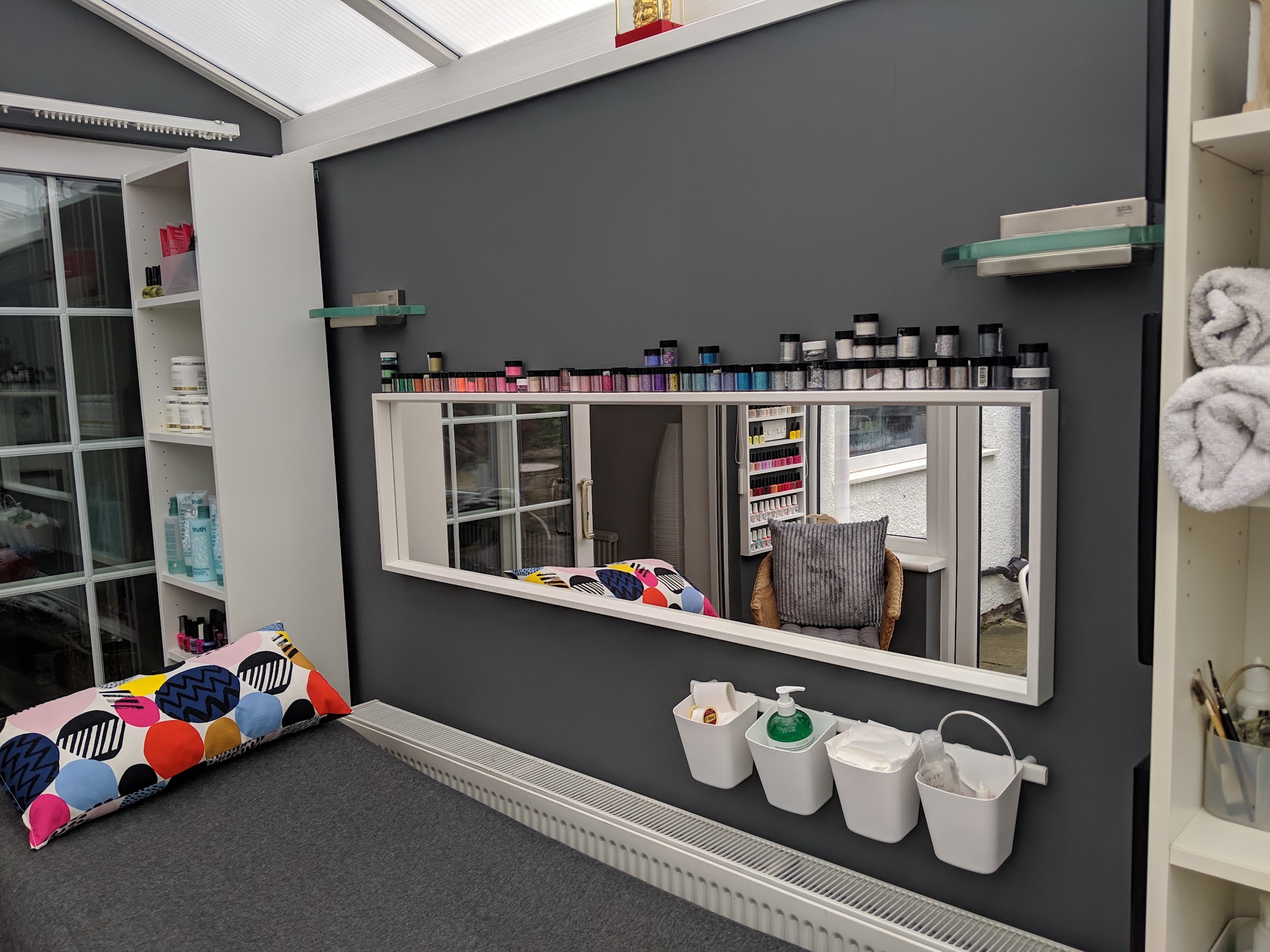 A mirror, treatment bed and shelves of nail colours inside the home salon
